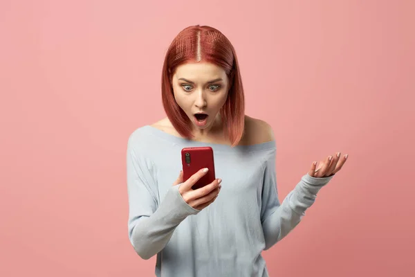 Surprised woman with phone in her hands standing in studio — Stock Photo, Image