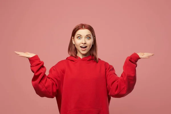 Jovem mulher gengibre em camisola vermelha com as mãos para cima isolado no fundo rosa no estúdio — Fotografia de Stock