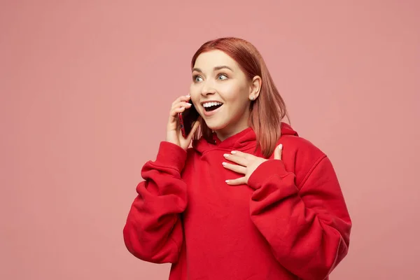 Glimlachend meisje in rode trui praten op telefoon geïsoleerd op roze achtergrond — Stockfoto