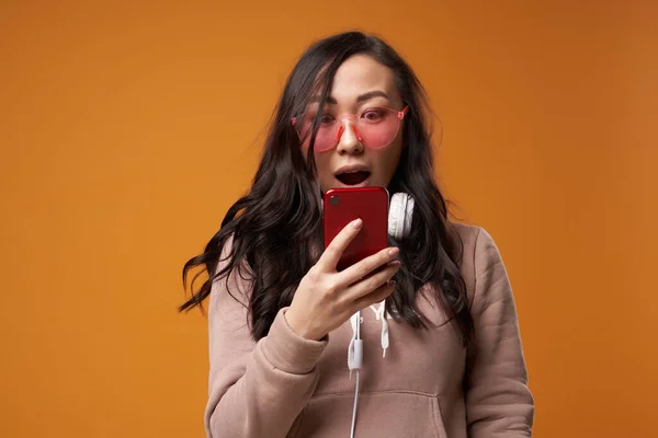 Asian woman in pink glasses with phone in her hands isolated in studio — Stock Photo, Image