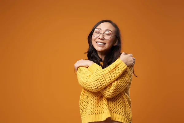 Χαρούμενη γυναίκα με γυαλιά αγκαλιάζει τον εαυτό της σε άδειο πορτοκαλί φόντο — Φωτογραφία Αρχείου