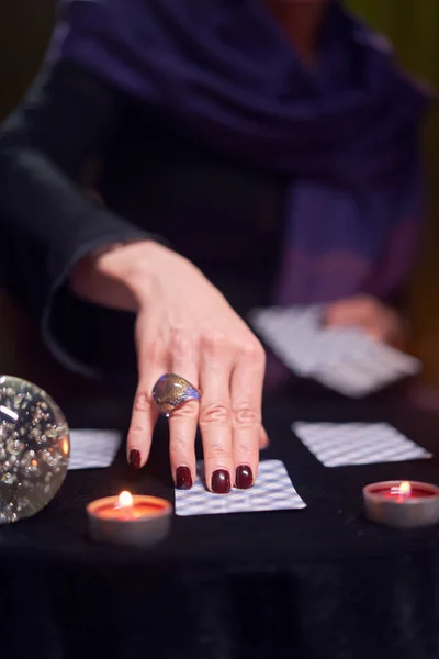 Primer plano de las adivinas mano con tarjetas de adivinación en la mesa con velas en la habitación oscura — Foto de Stock