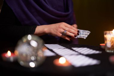 Mor elbiseli falcı kadın masada mumlarla oturuyor.