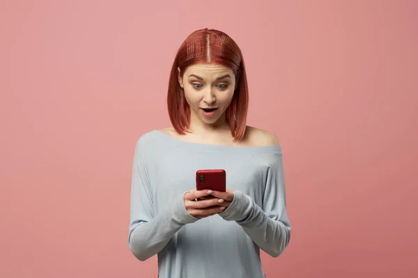 Serious ginger woman with phone in her hands standing in studio — Stock Photo, Image