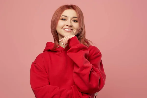 Glimlachend meisje in rood sweatshirt geïsoleerd leeg roze achtergrond in studio — Stockfoto