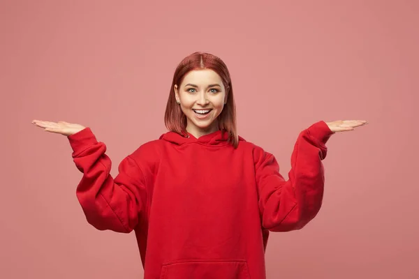 Mujer jengibre en suéter rojo con las manos arriba aislado sobre fondo rosa en el estudio — Foto de Stock