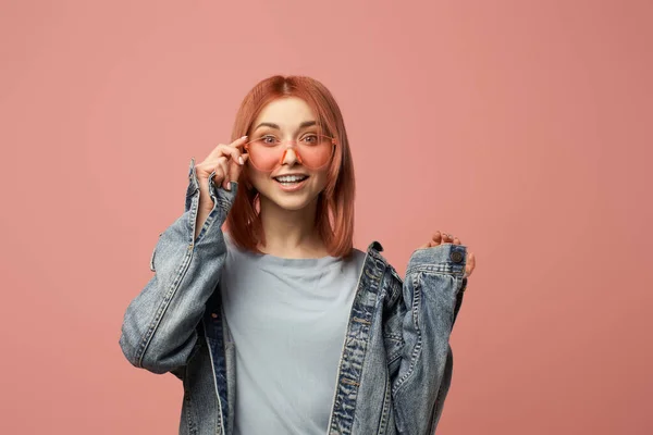 Χαμογελαστή γυναίκα με ροζ γυαλιά και τζιν σακάκι στέκεται στο στούντιο — Φωτογραφία Αρχείου