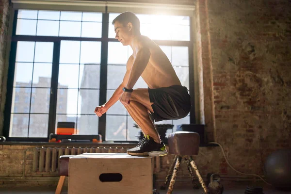 Vista lateral de atleta de salto en caja de madera en gimnasio contra fondo de ventana grande — Foto de Stock