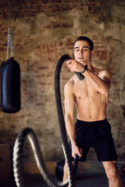 Esportista em treinamento com cordas contra fundo de parede de tijolo no ginásio — Fotografia de Stock