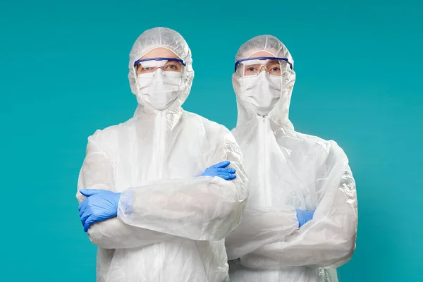 Twee medici in beschermende pakken met maskers geïsoleerd op blauwe achtergrond. Epidemisch pandemisch coronavirusconcept. — Stockfoto