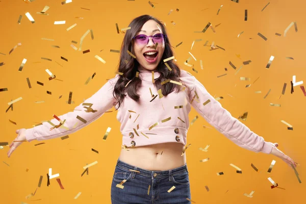 Mujer asiática alegre en gafas púrpura con confeti sobre fondo naranja —  Fotos de Stock