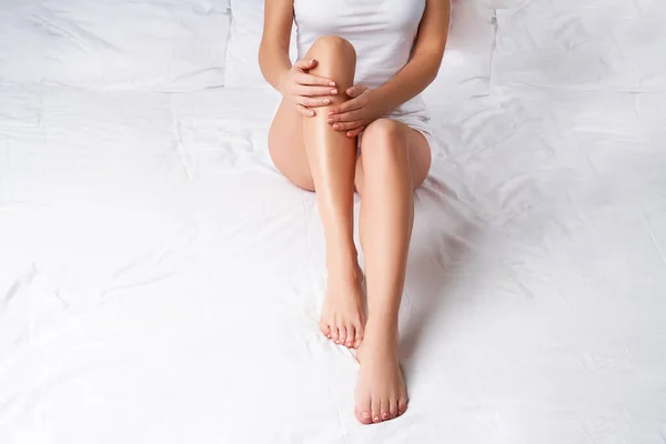 Vrouw raakt gladde huid van haar benen in bed, — Stockfoto