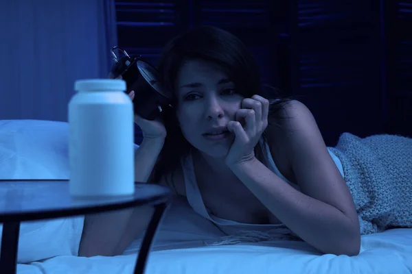 Chica infeliz con insomnio acostado en la cama junto al despertador y lata de leche por la noche . —  Fotos de Stock