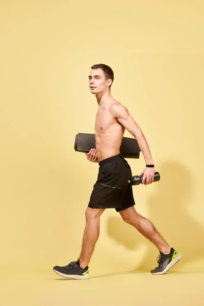 Joven atleta con alfombra caminando en estudio — Foto de Stock