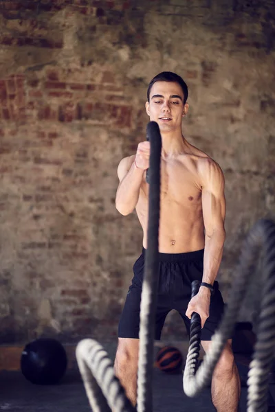 Jovem desportista em treinamento com cordas contra fundo de parede de tijolo — Fotografia de Stock