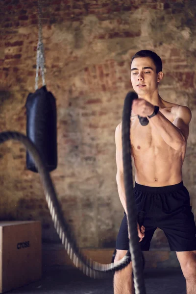 Hombre atleta joven en el entrenamiento con cuerdas contra el fondo de la pared de ladrillo, saco de boxeo — Foto de Stock