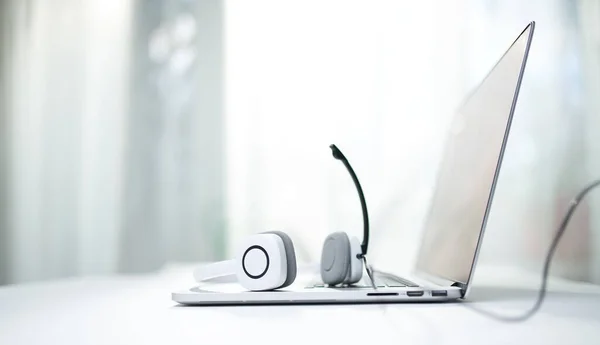 Primo piano del computer portatile, cuffie bianche con microfono su sfondo bokeh . — Foto Stock