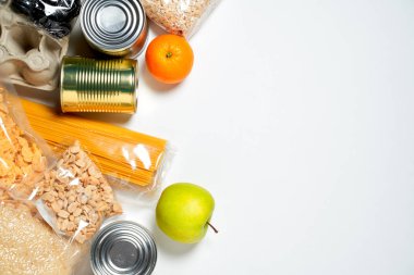 Beyaz arka planda plastik poşetlere, konservelere ve meyvelere kapatılmış çeşitli yiyecekler..