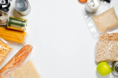 Beyaz arka planda plastik poşetlere, konservelere ve meyvelere kapatılmış çeşitli yiyecekler..