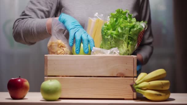 Fechar as mãos em luvas de proteção colocando alimentos em uma caixa de doação . — Vídeo de Stock