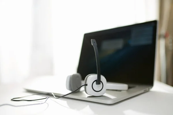 Ordenador portátil con pantalla negra, auriculares, micrófono en la mesa sobre fondo borroso . — Foto de Stock