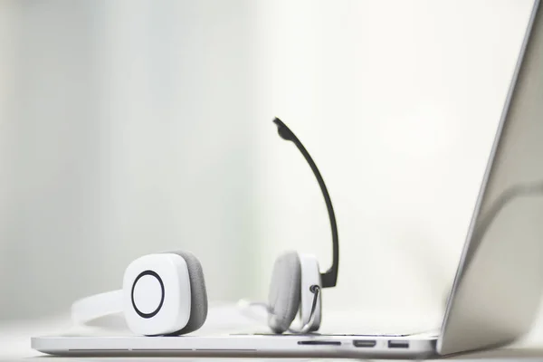 Primer plano del portátil, auriculares blancos con micrófono sobre fondo borroso . —  Fotos de Stock