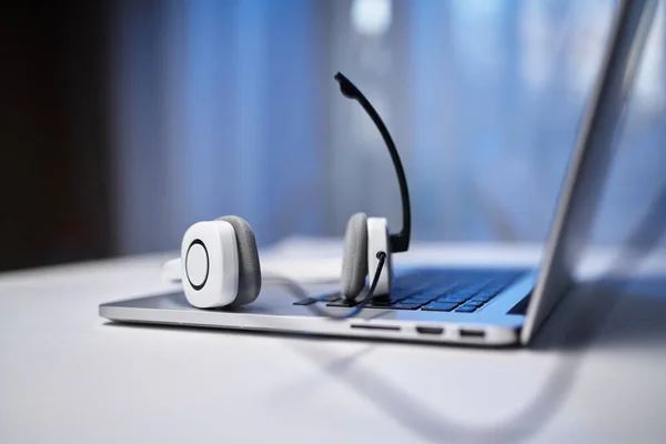 Laptop, weiße Kopfhörer mit Mikrofon auf verschwommenem blauem Hintergrund. — Stockfoto