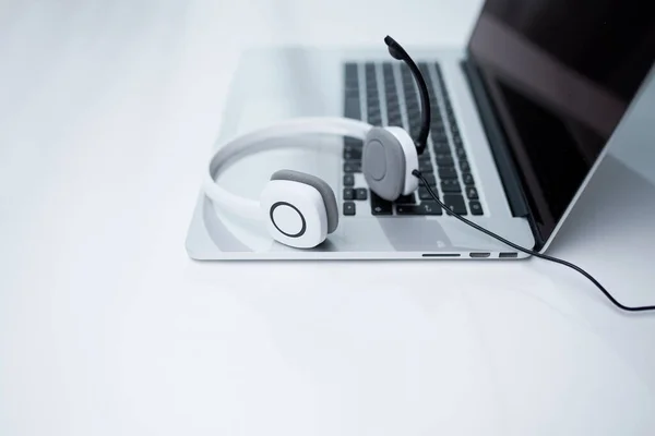 Laptop, białe słuchawki z mikrofonem na stole. — Zdjęcie stockowe