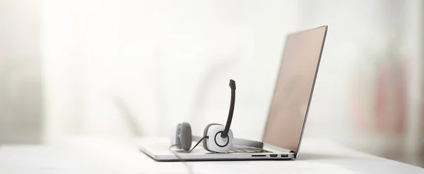 Laptop, weiße Kopfhörer mit Mikrofon auf dem Tisch defokussierter Hintergrund. — Stockfoto