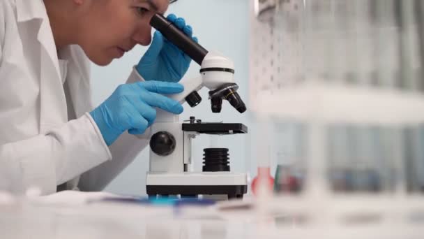 Női orvosi kutató kutató, aki mikroszkóppal nézi. — Stock videók