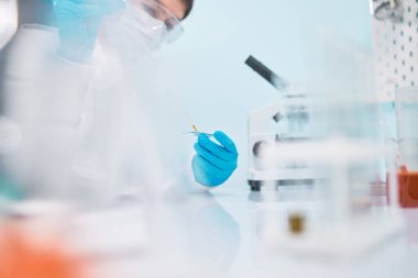Pipetli, bulanık arka planlı, güvenlik gözlüklü kadın laboratuvar teknisyeni..