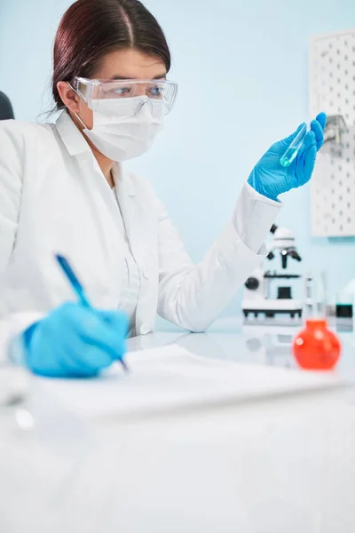Techniczka laboratoryjna z probówką w ręku robi notatki. Epidemia koronawirusa — Zdjęcie stockowe