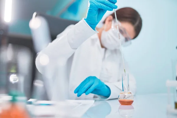 Woman lab technician with pipette and flask, blurred background. — Stock Photo, Image