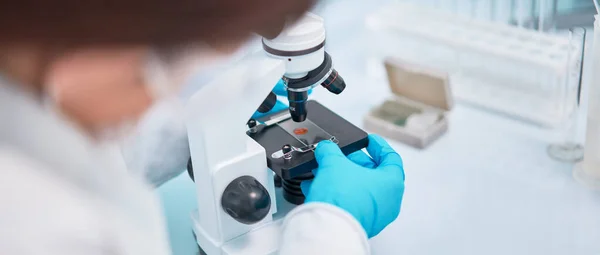Close-up van de vrouw lab assistent in blauw rubber handschoenen op zoek door de microscoop. — Stockfoto