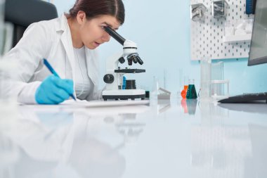 Laboratuvar teknisyenlerinin mavi lastik eldivenleriyle laboratuarda mikroskoba baktığı yeri kapatın..