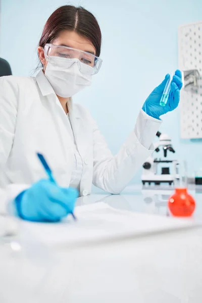 Female lab technician with test tube in hand makes note. — Stock Photo, Image