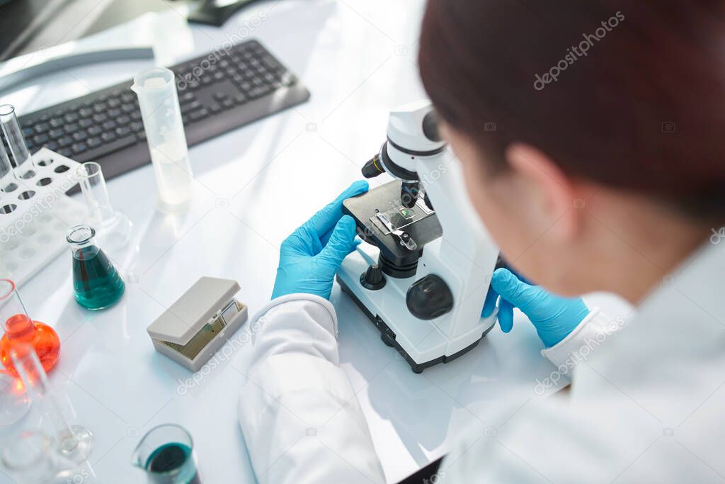 Female laboratory assistant looking through microscope in laboratory, closeup.