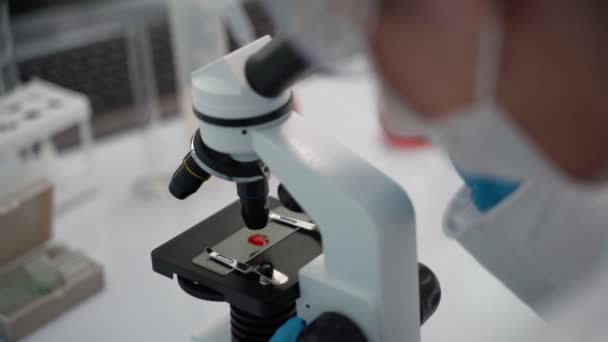 Mujer Científica mirando a través de un microscopio en un laboratorio . — Vídeo de stock