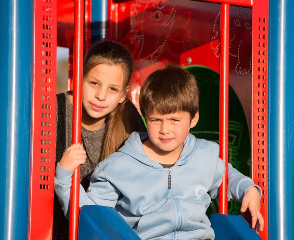 Ragazza e ragazzo seduto sul parco giochi — Foto Stock