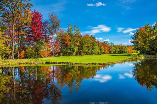 Shining sunny day in French Canada. Red, orange and yellow autumn foliage reflected in the clear water of the lake. Concept of recreational tourism. Park fantastic beauty