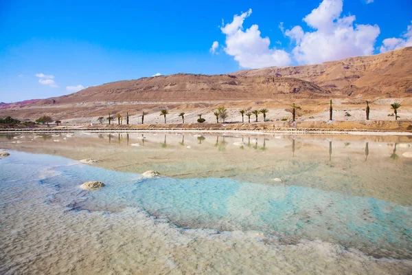 Midday heat evaporates water. Between the sea and dry mountains of red sandstone highway passes. Turquoise water of the Dead Sea, Israel. The concept of medical and ecological tourism