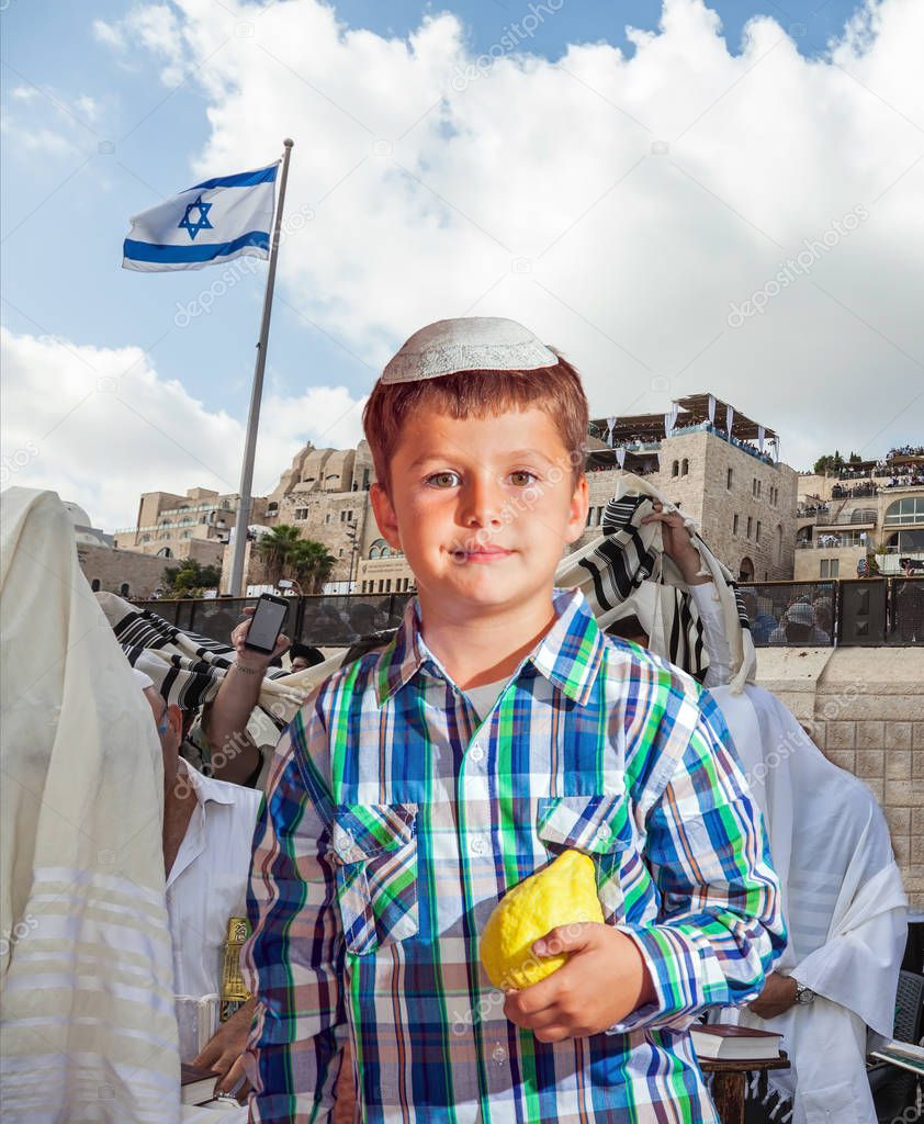 Autumn Jewish holiday Sukkot. People in white Taliths pray at the Western Wall of the Temple. Beautiful Jewish boy in white skullcap, with etrog