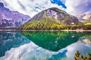 Magnificent lake Lago di Braies. South Tyrol, Italy. Emerald expanse of water reflects the surrounding forest and mountains. The concept of walking and eco-tourism clipart