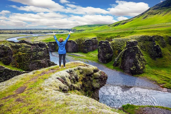 The elderly woman - tourist in blue jacket, admiring the magnificent scenery. Green Tundra in summer.  The concept of active northern tourism. The striking canyon in Iceland