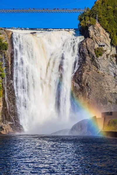 Magnificent rainbow in the spray of the waterfall Montmorency in Montmorency Falls Park, in Quebec.  Above the waterfall built bridge for walking. The concept of active and cultural tourism