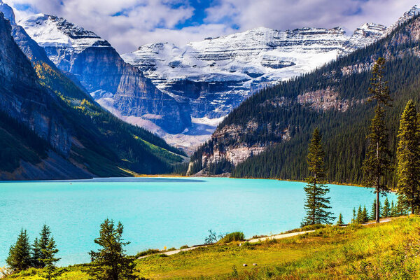 Travel to the Rocky Mountains of Canada. The lake with azure water is surrounded by mountains and forests. Glacial Lake Louise. Sunny fine day. The concept of ecological, active and photo tourism