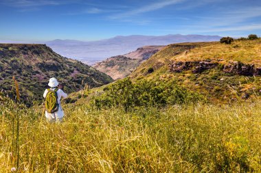 Beyaz şapkalı sırt çantalı kadın resimli manzara. İsrail 'de Yahudi Paskalyası. Bahar çiçekleri açan Golan Tepeleri volkanik kökenli bir dağ yaylası. Ekolojik, aktif ve fotoğraf turizmi kavramı
