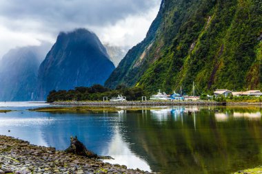 Hobbitler ve cinler ülkesi. Milford Sound 'un ünlü okyanusu üzerindeki fırtına bulutları gökyüzünü kaplıyor. Turist gemileri, yatlar ve tekneler. Egzotik ve fotografik turizm kavramı. Yeni Zelanda