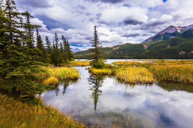 Gölün yumuşak suyu bulutlu gökyüzünü yansıtır. Kanada 'nın Rocky Dağları' nda muhteşem bir yolculuk. Aktif ve ekolojik turizm kavramı