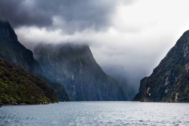 Yeni Zelanda. Antarktika 'dan esen soğuk rüzgar Milford Sound fiyortlarının suyunu dalgalandırıyor. Ağır, kasvetli bulutların arasından, güneşin ışınları yolu açar. Egzotik, aktif ve fotografik turizm kavramı